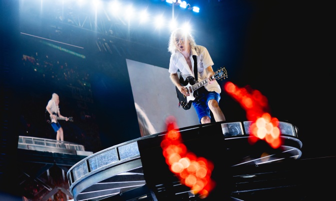 Der Gitarrist von AC/DC schaut direkt in die Kamera, im Vordergrund sind Flammen zu sehen.