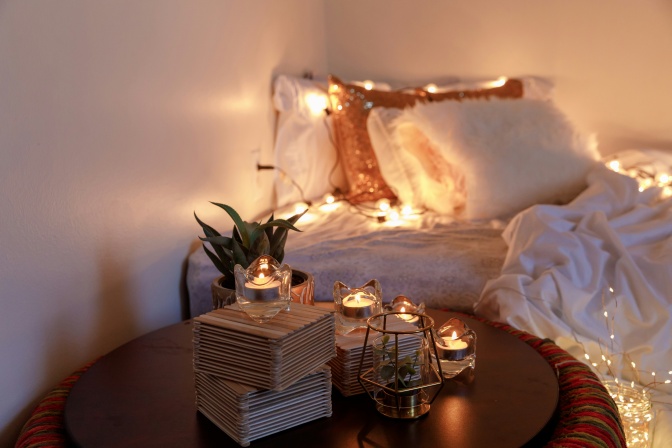 Kerzen und Lichterketten machen gemütliches Licht um ein Bett herum.