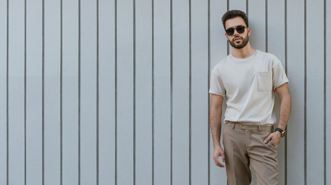 Ein Mann mit Vollbart und Sonnenbrille lehnt lässig an einer Bretterwand.