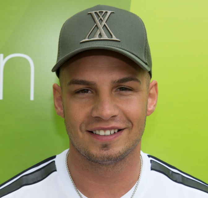 Pietro Lombardi mit einer grünen Schirmmütze vor einer Logowand des ZDF Fernsehgartens