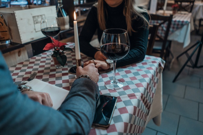 Ein Mann und eine Frau sitzen an einem Tisch und halten Händchen. Zwischen ihnen stehen rote Rosen.