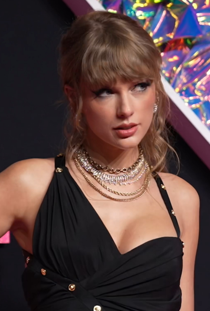 Taylor Swift in einem asymmetrischen schwarzen Kleid mit gewellten, hochgesteckten Haaren.