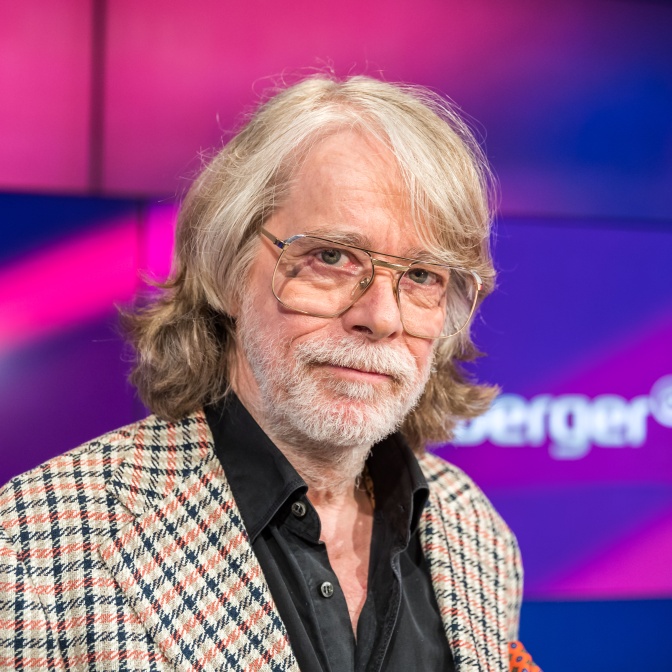 Helge Schneider mit längeren grauen Haaren und Vollbart. Er schaut seitlich an der Kamera vorbei.
