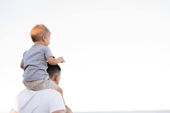 Ein Mann trägt ein Kleinkind auf den Schultern. Die beiden wurden von hinten fotografiert.