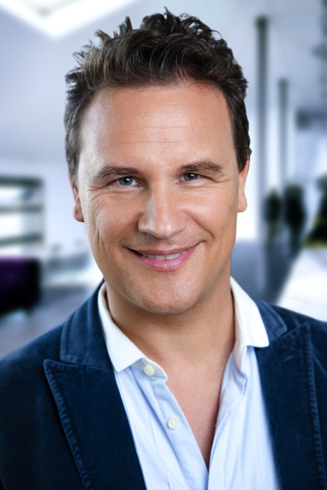 Guido Maria Kretschmer in einem weißen Hemd mit blauem Sakko. Er schaut direkt in die Kamera.