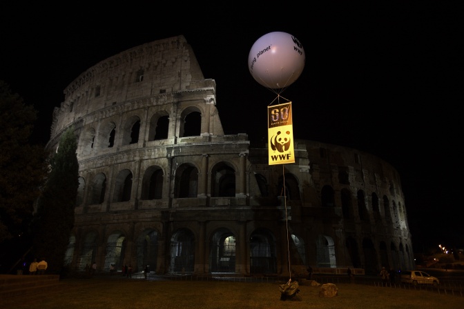 Schemenhafte Umrisse des Kolossseums im Dunkeln, im Vordergrund eine Infotafel des WWF zur Earth Hour.
