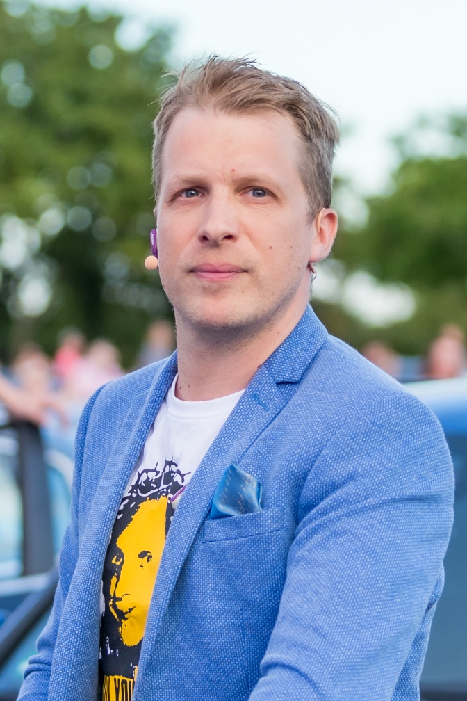 Oliver Pocher in einem hellblauen Anzug und einem T-Shirt mit Print. Er schaut mit ernstem Blick direkt in die Kamera.