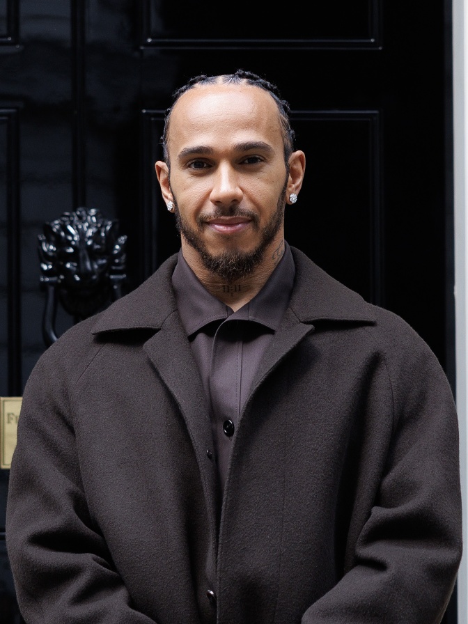 Lewis Hamilton in einem schwarzen Mantel mit Braids und Vollbart.