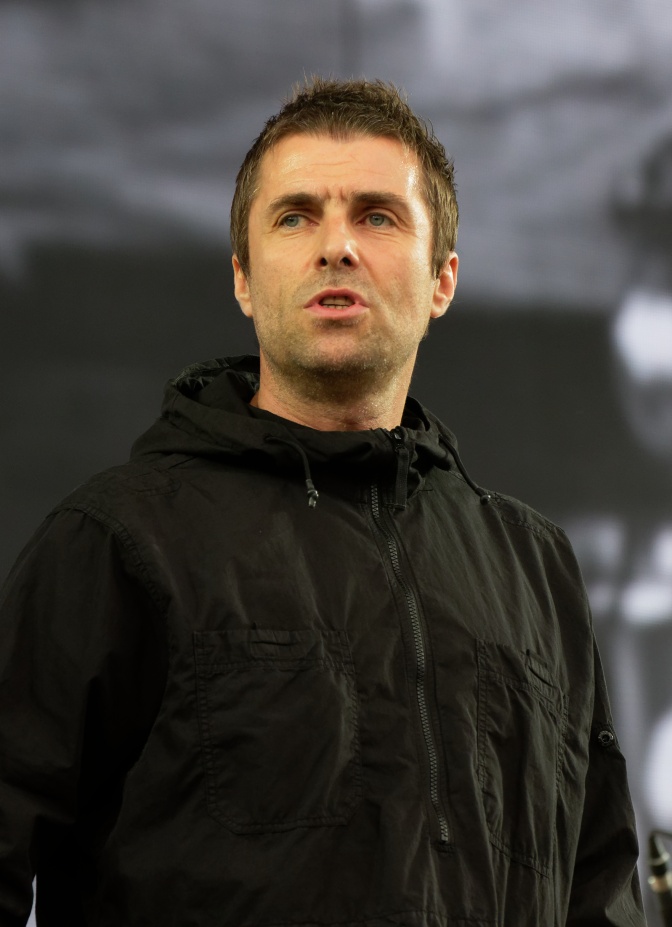 Liam Gallagher in schwarzer Kleidung. Er schau mit ernstem Blick leicht an der Kamera vorbei.