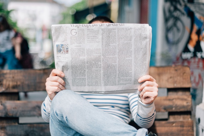 Ein Mann sitzt im Freien auf einer Bank und liest eine Zeitung.
