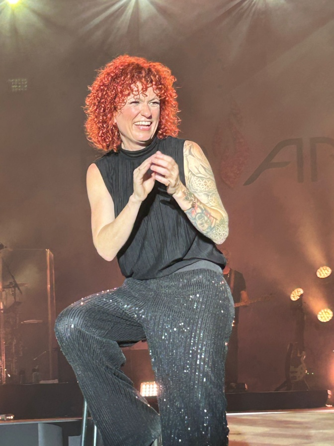 Lucy Diakovska sitzt auf einem hohen Barhocker auf der Bühne und  lacht.