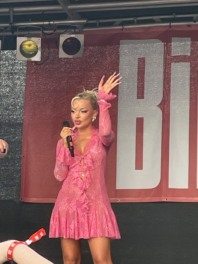 Katja Krasavice steht winkend auf einer Bühne, hinter ihr das Logo der Bild-Zeitung