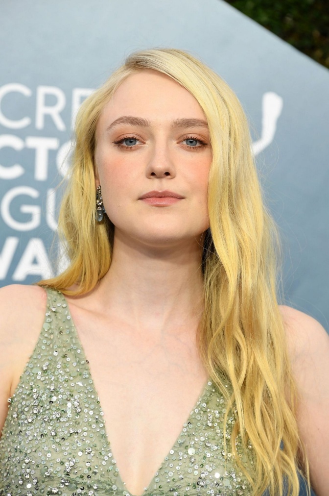 Dakota Fanning in einem glitzernden türkisfarbenen Kleid vor einer Logowand.