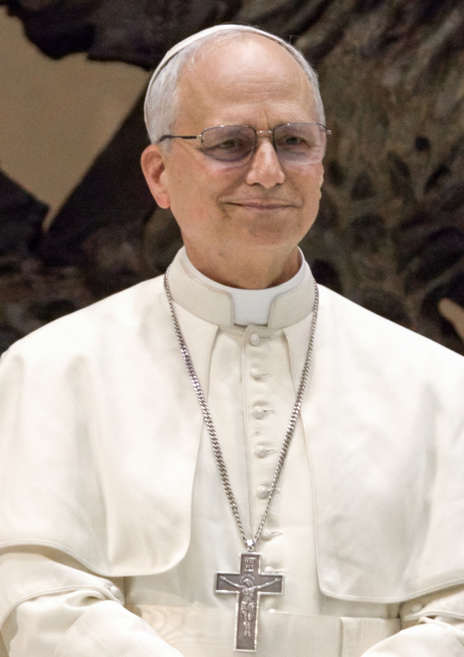 Papst Leo in weißer Kleidung mit einer kleinen, weißen Kappe auf dem Kopf. Er trägt eine große Kette mit einem Kreuz.