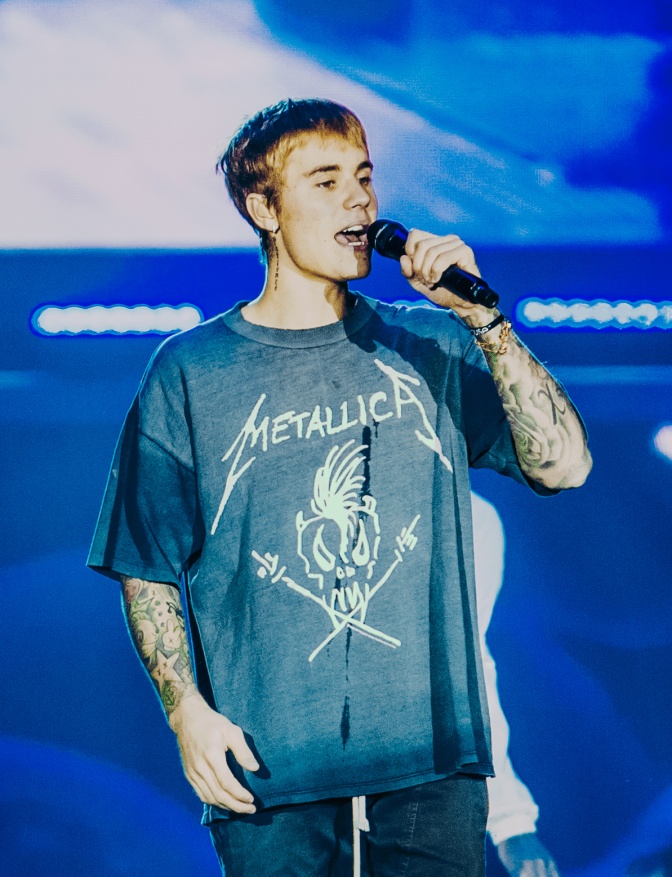 Justin Bieber steht in einem blauen Metallica-T-Shirt auf der Bühne und singt in ein Mikro.