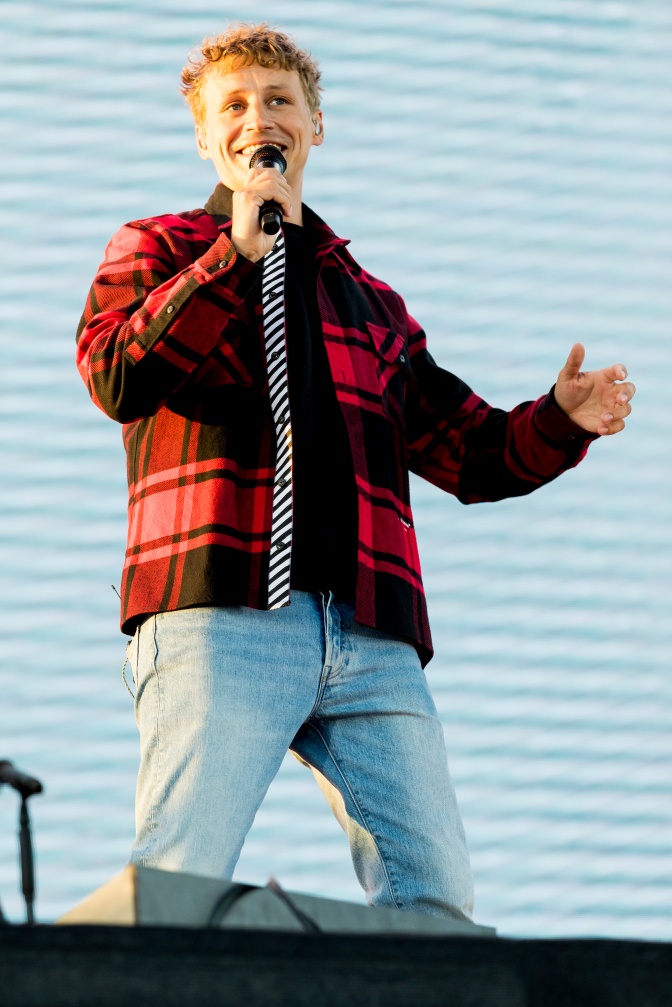 Tim Bendzko in Jeans und Holzfällerhemd auf der Bühne. Er singt in ein Mikro und gestikuliert mit den Armen.