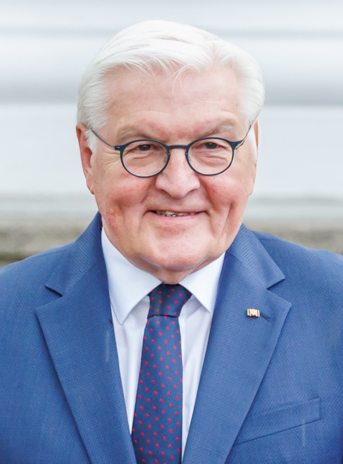 Frank-Walter Steinmeier mit weißen Haaren und Brille. Er trägt einen blauen Anzug und eine blaue Krawatte und lächelt in die Kamera.