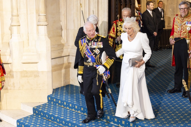 König Charles und Königin Camilla gehen in sehr festlicher Kleidung eine Treppe herunter.