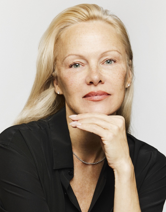Pamela Anderson mit dezentem Make Up und langen, glatten hellblonden Haaren. Sie hat den Kopf leicht in die Hand gestützt.