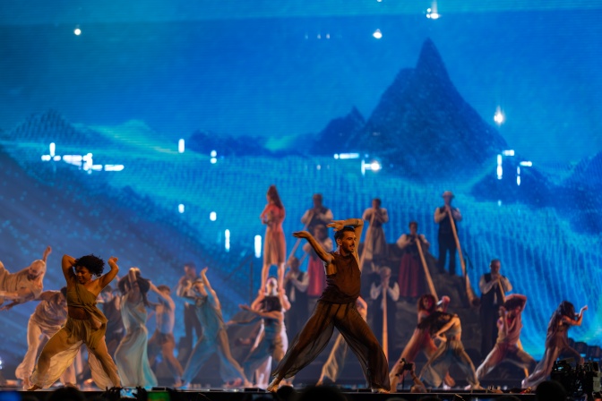 Tänzer*innen und Musiker*innen mit Alphörnern auf einer blau beleuchteten Bühne