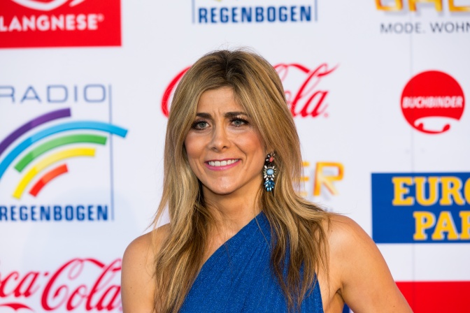 Panagiota Petridou in einem blauen, asymmetrischen Kleid vor einer Logowand.