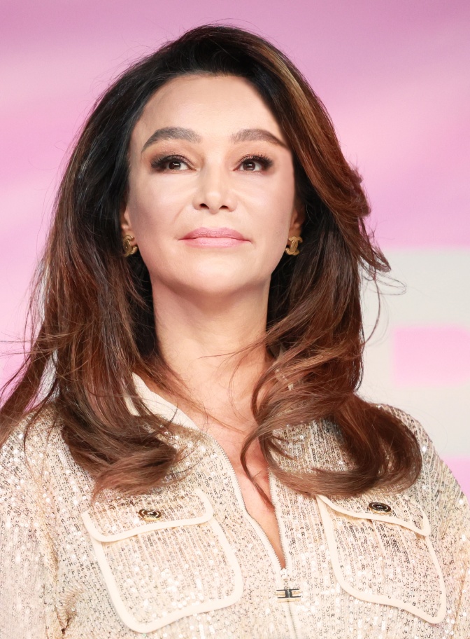 Verona Pooth in einer Boucléjacke mit Pailletten. Sie ist stark geschminkt und schaut leicht oberhalb an der Kamera vorbei.