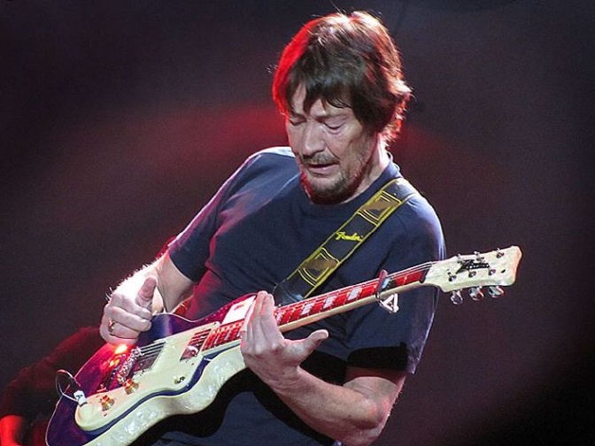 Chris Rea spielt mit hab geschlossenen Augen E-Gitarre. Die Bühne ist rot beleuchtet.