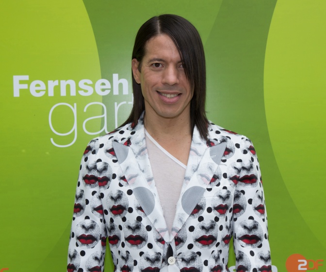 Jorge González in einem gemusterten Anzug vor einer Logowand des ZDF Fernsehgartens.
