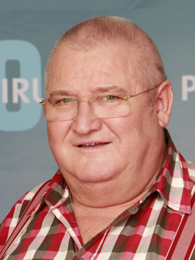 Horst Krause in einem Karohemd vor einer Logowand von Polizeiruf 110.