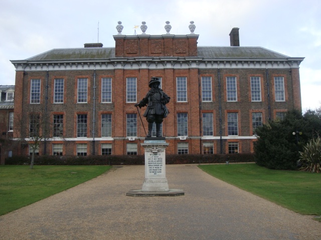 Ein kleines Schloss in Backsteinoptik mit hohen Sprossenfenstern. Davor steht eine Statue.