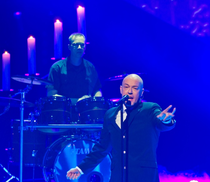 Die Band UNHEILIG auf der Bühne. Der Graf steht am Mikrofon, hinter ihm ist der Schlagzeuger zu sehen. Die Bühne ist blau beleuchtet.