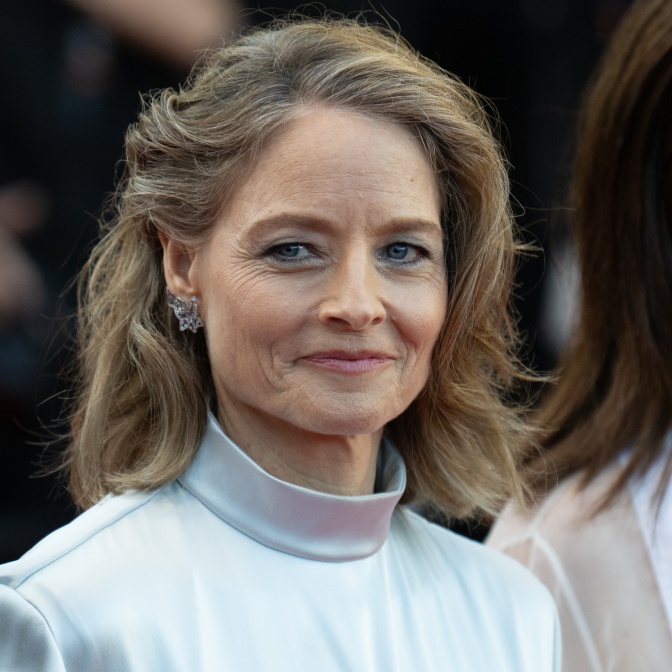 Jodie Foster hat einen Teil ihrer Haare seitlich zurückgesteckt und trägt dezentes Make up. Sie schaut direkt in die Kamera und lächelt leicht.