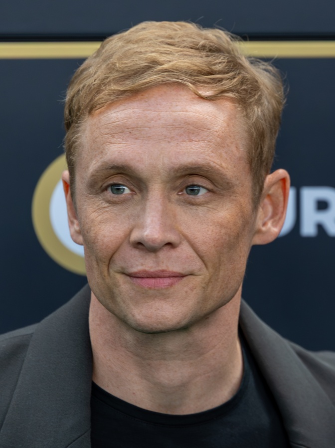 Matthias Schweighöfer steht vor einer Logowand und schaut mit ernstem Blick leicht seitlich an der Kamera vorbei.