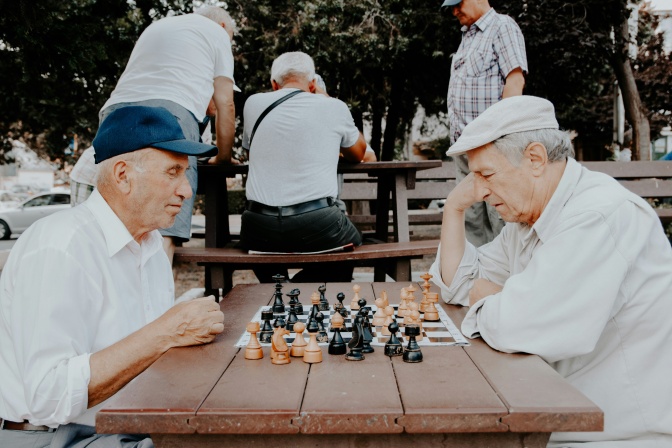 2 alte Männer sitzen im Freien zusammen und spielen Schach.