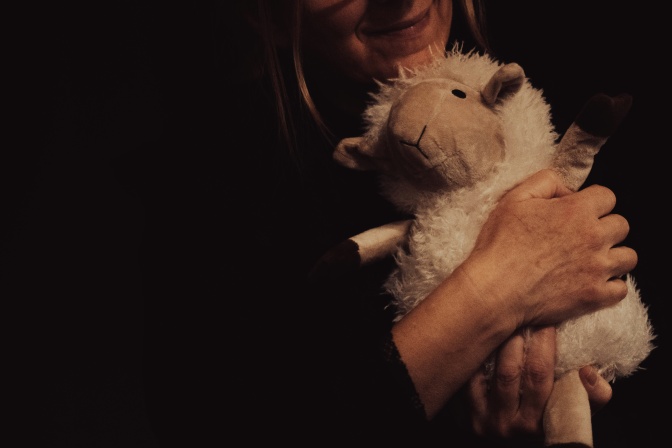 Eine erwachsene Frau kuschelt mit einem Plüschschaf. Ihr Gesicht ist auf dem Foto nicht zu sehen.