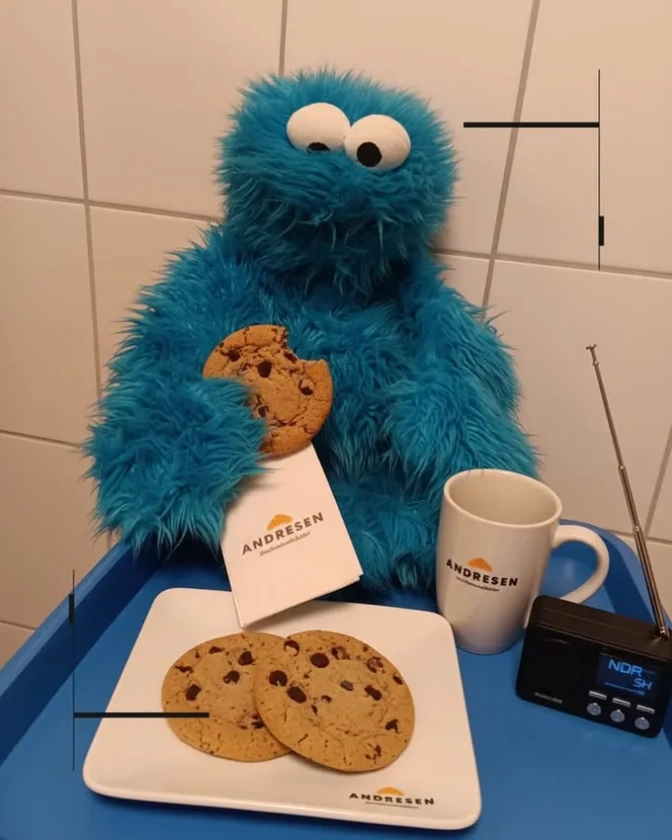 Eine Krümelmonsterpuppe sitzt vor einer gefließten Wand. Es hat einen Keks in der Hand, neben ihm steht ein Radio.