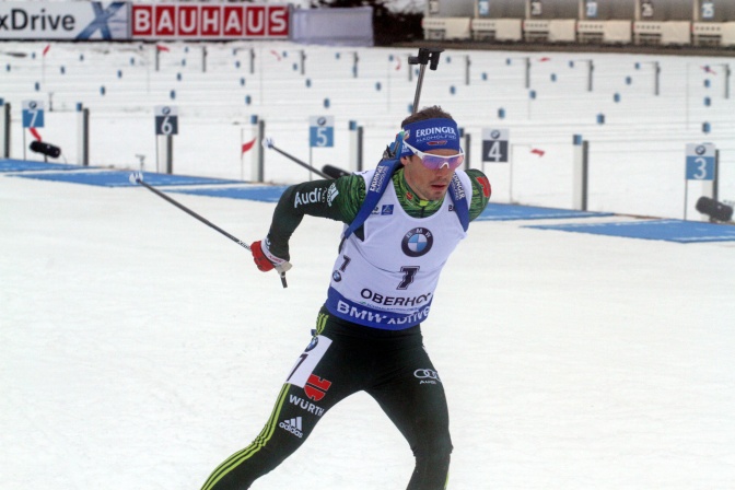 Simon Schempp auf der Skipiste. Sein Gewehr hat er auf dem Rücken. Er trägt Helm und Trikot.
