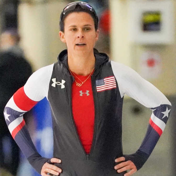 Brittany Bowe in einem Sportoutfit. Sie hat die Arme in die Seiten gestemmt undschaut direkt in die Kamera.