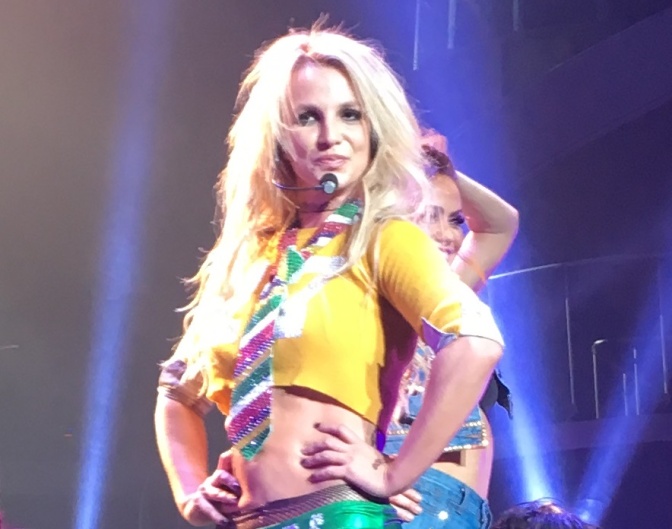 Britney Spears auf der Bühne in einem gelben Coop Top mit einer glitzernden Krawatte.