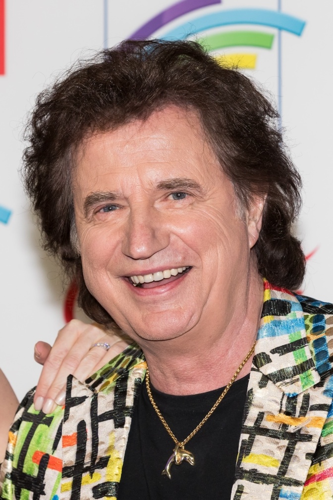 Olaf der Flipper mit dunklem Vokuhila in einem Hawaiihemd. Er lächelt in die Kamera. Um den Hals trägt er eine Goldkette mit einem Delfin.