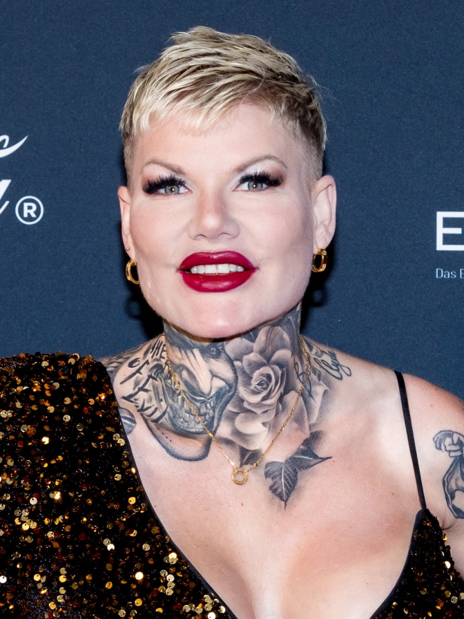 Melanie Müller mit kurzen blondierten Haaren, starkem Make up und einem großen Halstattoo. Man sieht: Sie hatte viele Schönheitsoperationen.