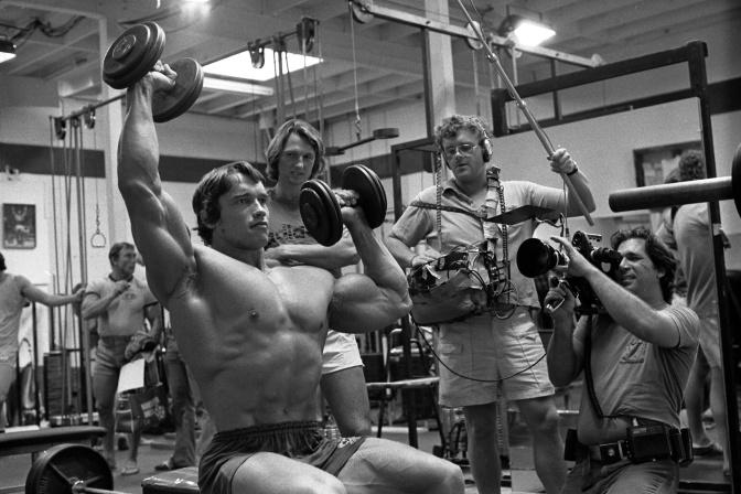 Schwarz-weiß-Foto von Arnold Schwarzenegger beim Training. Er ist noch sehr jung und hat große Muskeln.
