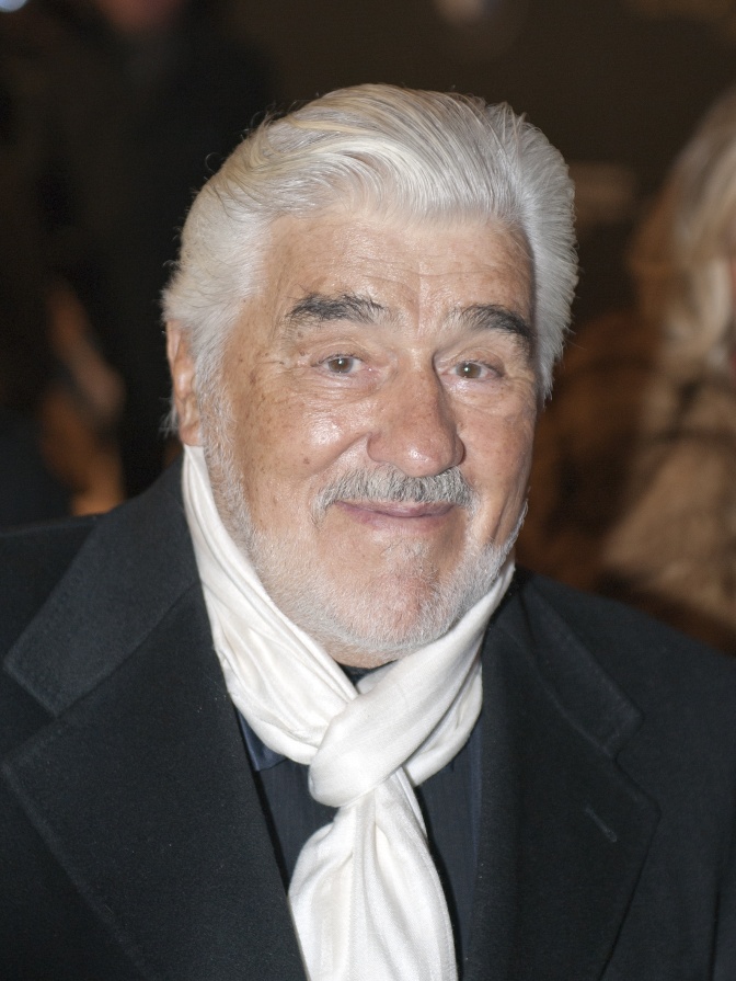 Mario Adorf mit weißen Haaren und weißem Bart. Er trägt einen weißen Schal und lächelt in die Kamera.
