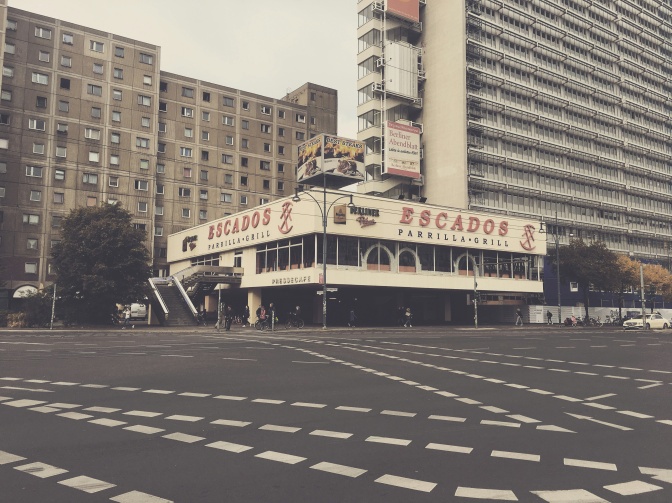 Ein verblichenes Foto wahrscheinlich aus den 1970er Jahren. Ein Auto ist an der Straße geparkt, im Hintergrund Gebäude.