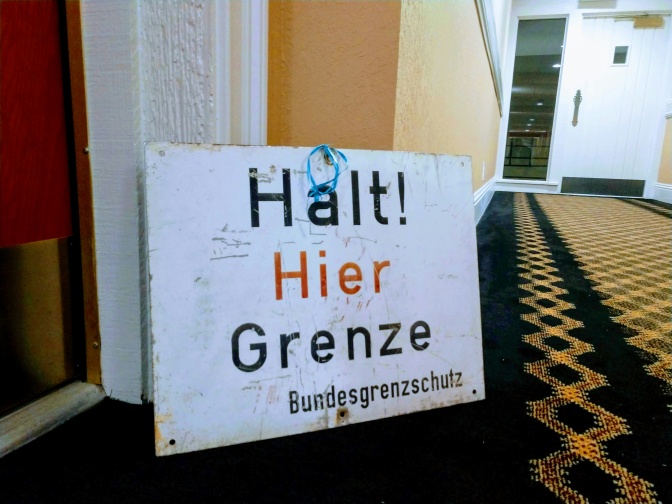 Ein Schild lehnt an der Hauswand. Darauf steht: Halt! Hier Grenze!