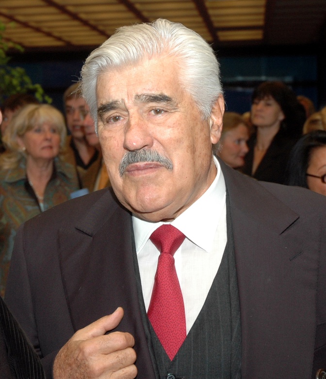 Mario Adorf im Anzug und mit roter Krawatte. Seine Haare sind weiß, hinter ihm steht eine Menschenmenge.