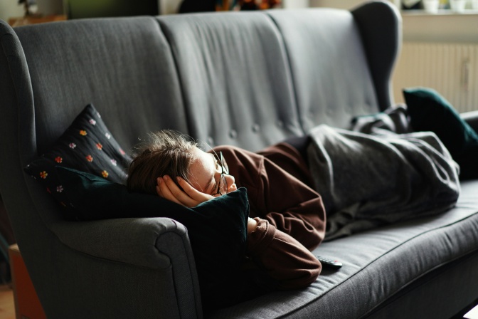 Eine Frau liegt auf der Couch und schläft. Sie hat dabei ihre Brille noch auf.