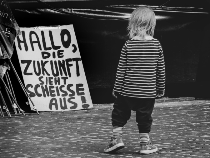 Schwarz-weiß-Foto: Ein kleines Mädchen steht vor einem Demoschild mit der Aufschrift: Hallo, die Zukunft sieht Scheiße aus.