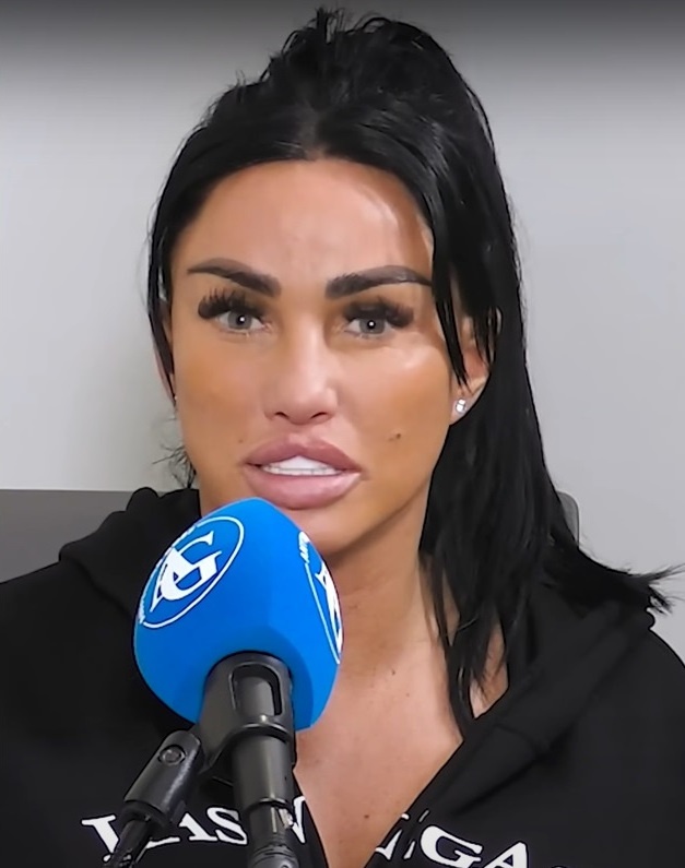 Katie Price sitzt vor einem Mikrofon und spricht. Sie hat dunkelbraune Haare und einen Pferdeschwanz. Ihre Lippen sind aufgespritzt.