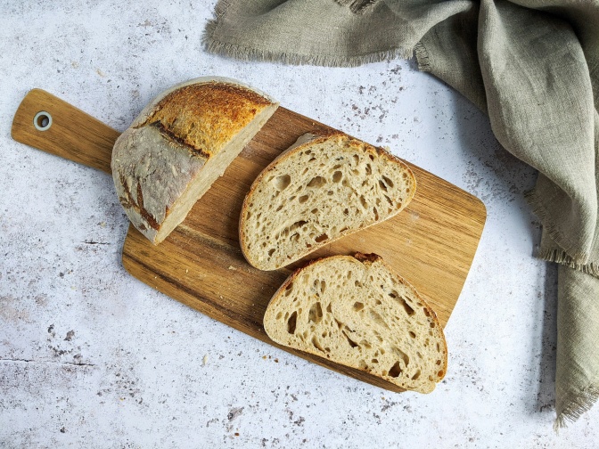 Ein halbes Brot auf einem Holzbrett, 2 Scheiben sind davon abgeschnitten.